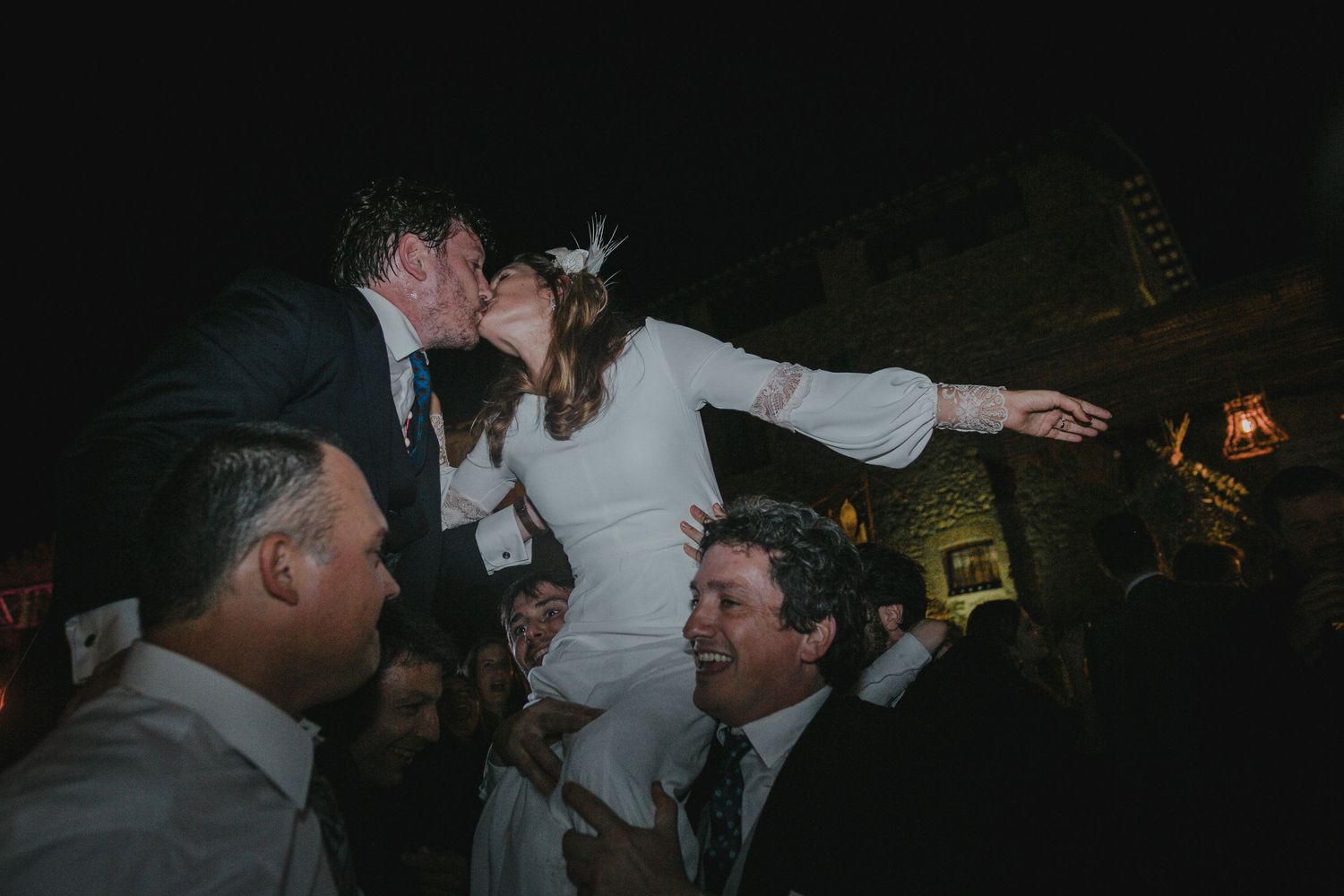 Wedding celebration with bride being lifted by guests during evening reception.