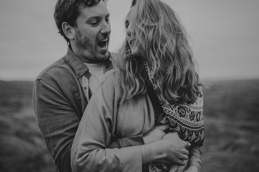 A joyful candid moment shared between two people on a cloudy hilltop.