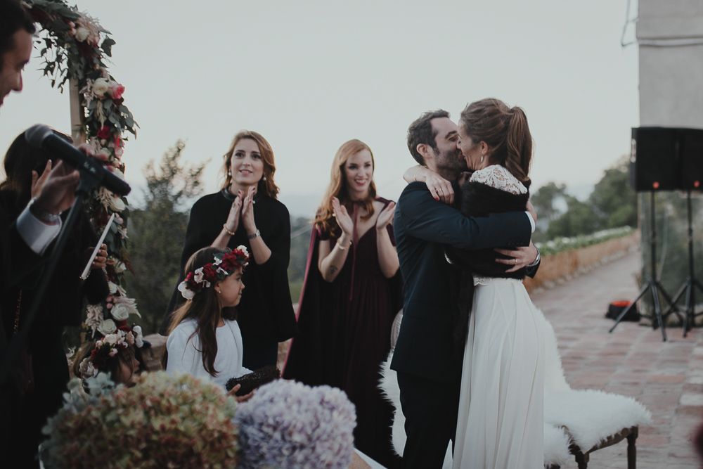 Wedding guests applaud during an emotional ceremony moment outdoors with floral decorations.