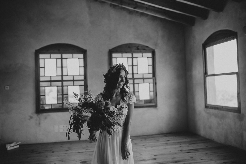 Silhouette holding floral bouquet against arched windows in empty room.