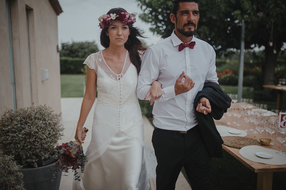 A couple in wedding attire walks arm in arm on stone patio.