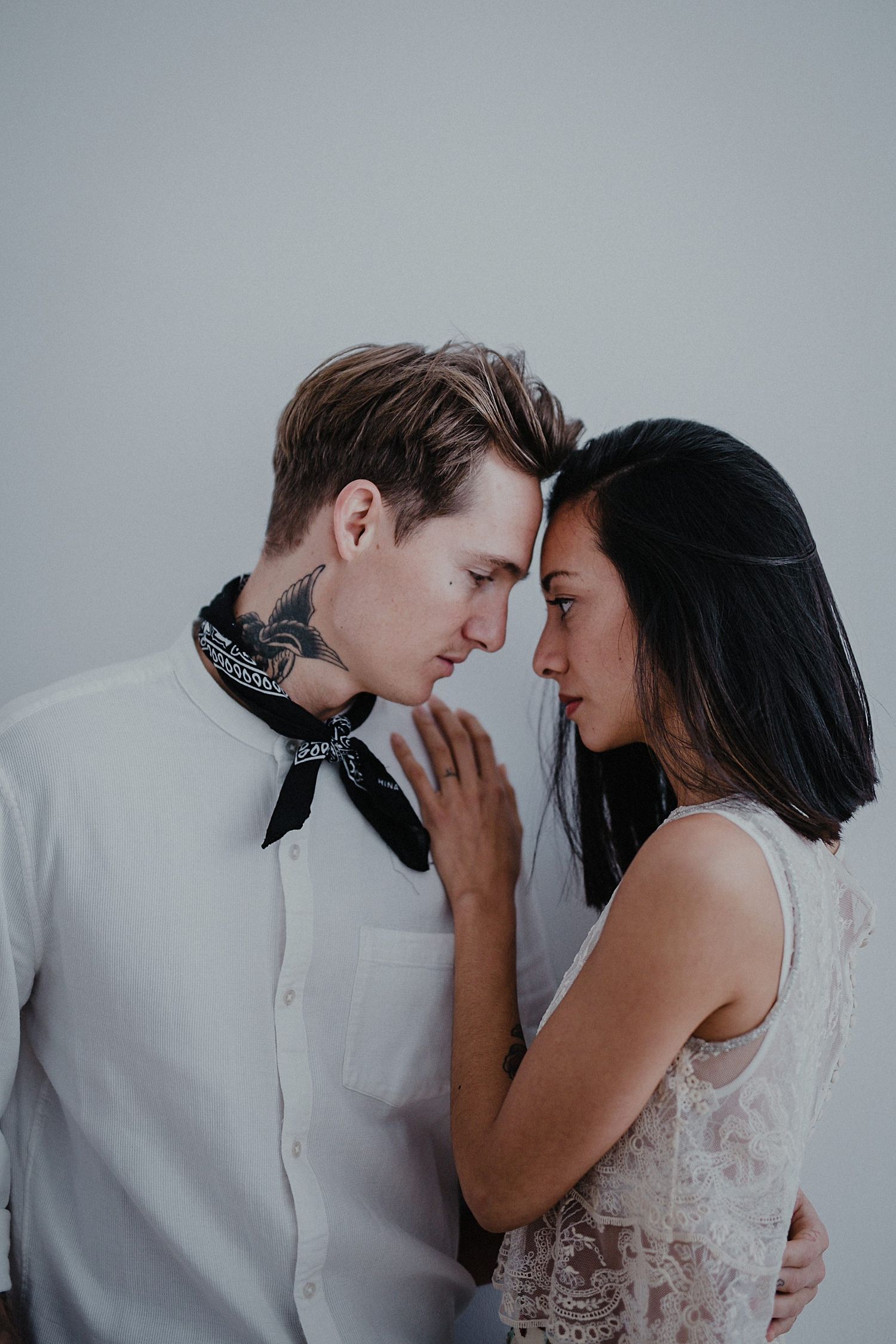 An intimate moment between a couple in white formal wear against a grey background.