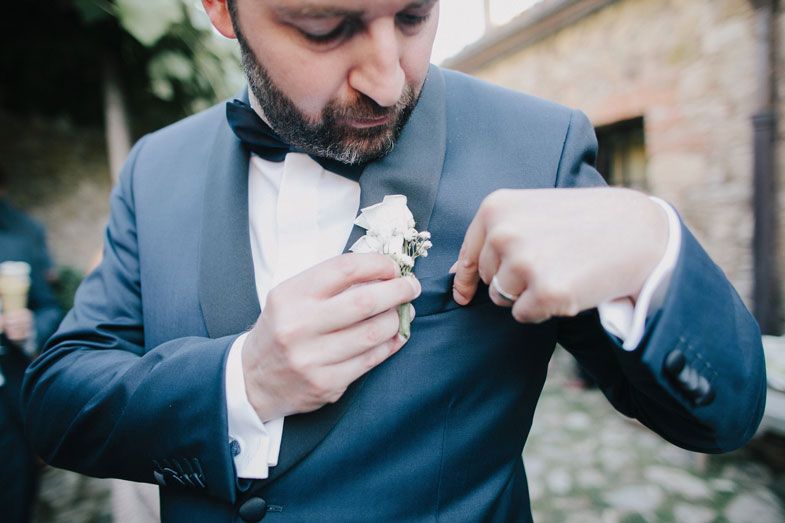 A gentleman in a blue suit adjusts his boutonniere at a formal event.