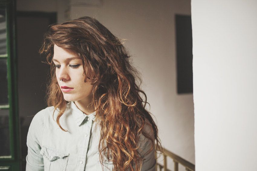 Side profile of person with wavy brown hair against white wall interior.