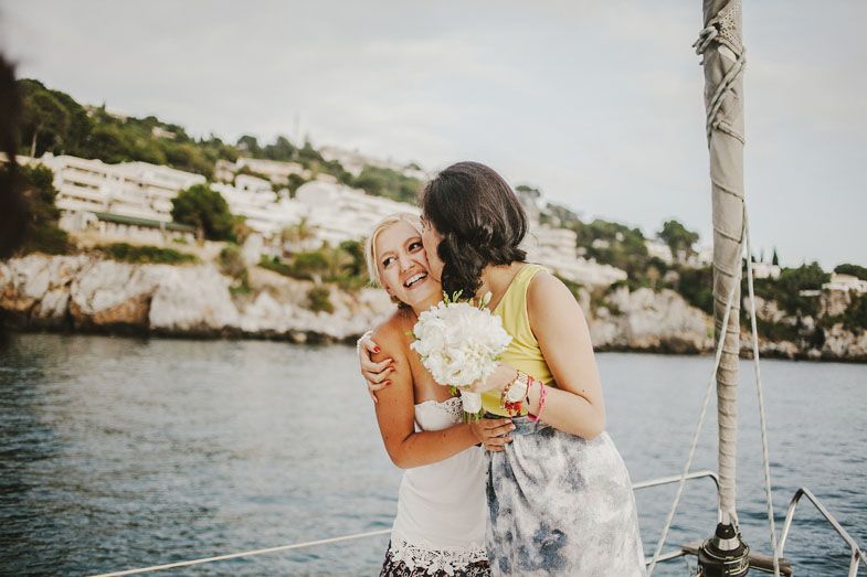 Two people embrace on a coastal clifftop while holding bouquets.