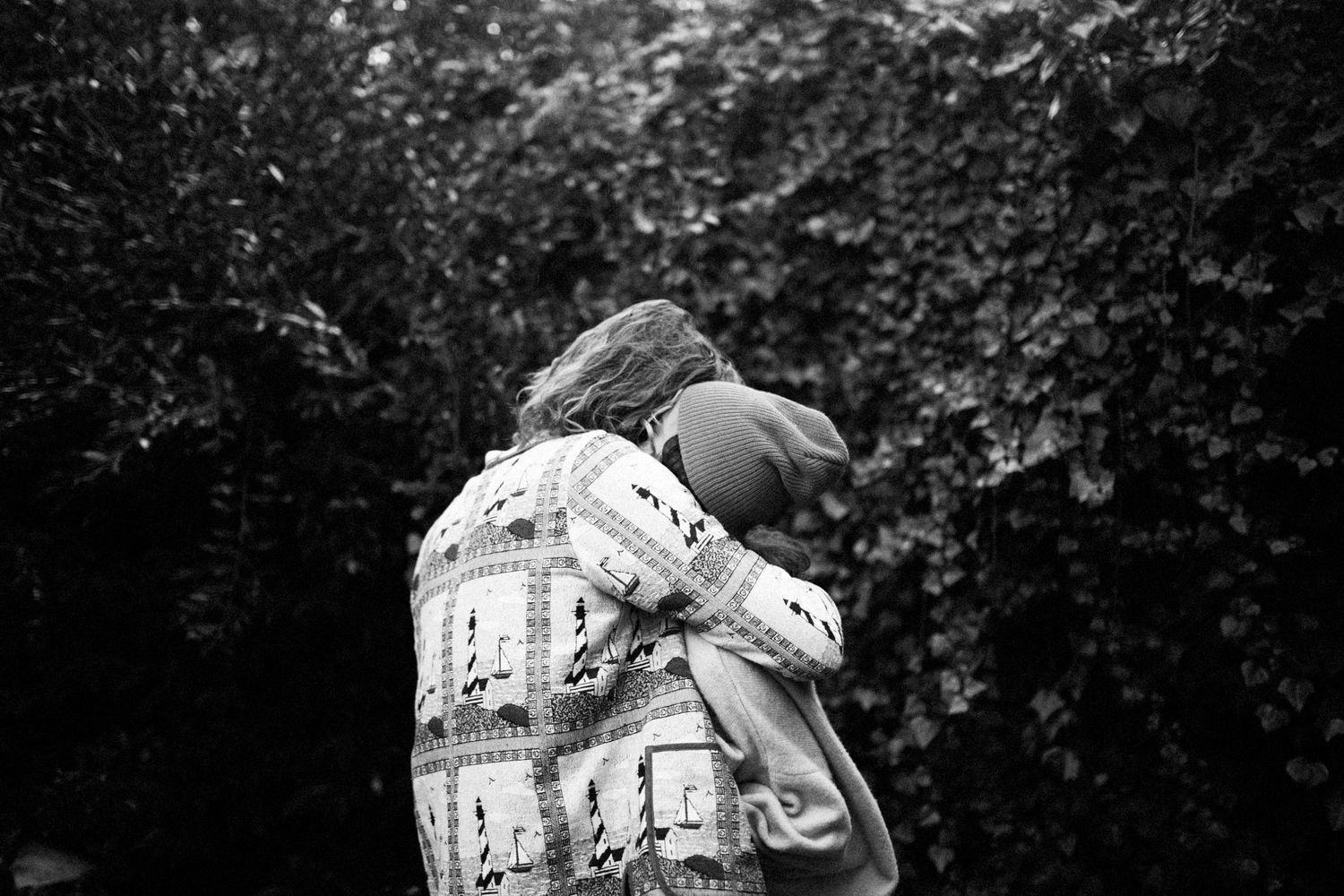 Black and white intimate embrace between a couple against a garden backdrop.