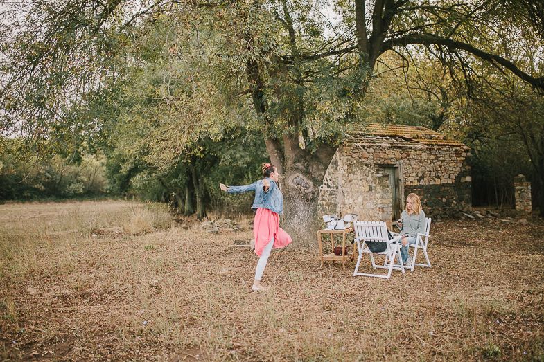 A pastoral garden scene with whimsical decor and white chairs arranged beneath autumn trees.