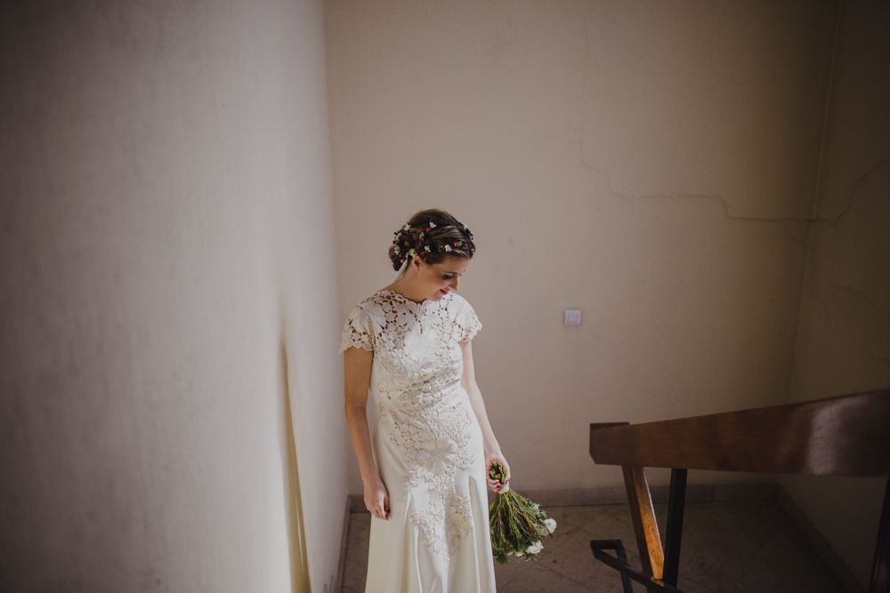 Elegant lace wedding gown with cap sleeves shown against a neutral wall.