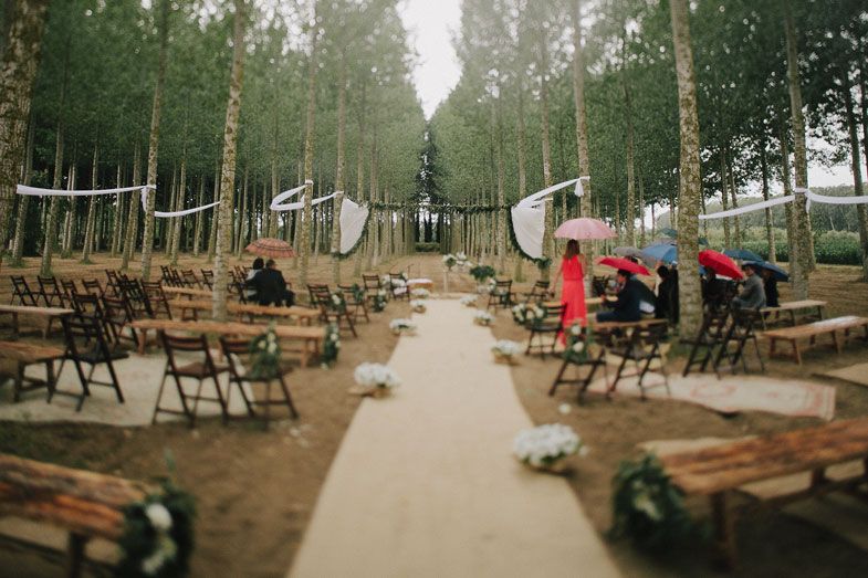 Rustic outdoor wedding ceremony setup with wooden benches in a forest setting.