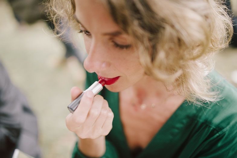 Close-up shot of someone applying lipstick while wearing an emerald green dress.