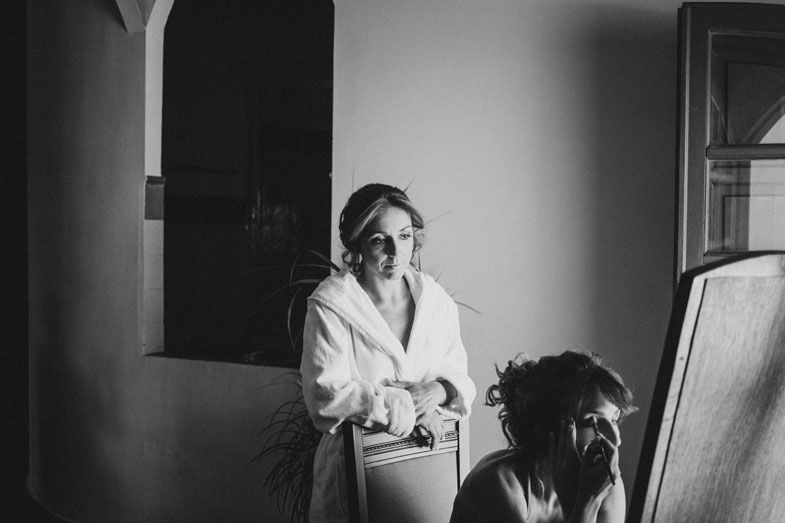 Candid black and white photo of bridal preparations near a window.