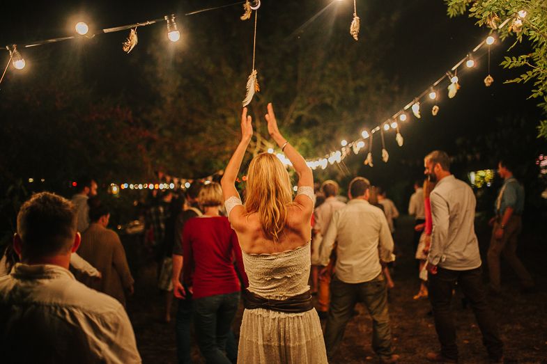 People dancing and celebrating under string lights at an outdoor nighttime gathering.