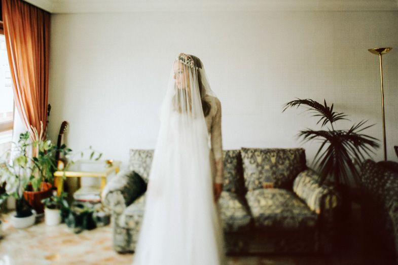A wedding veil hangs elegantly in front of a floral couch and potted palm.