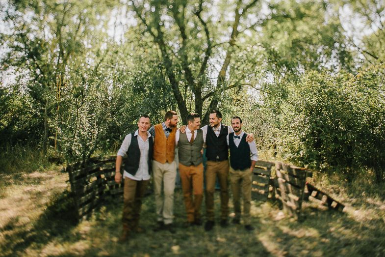 Group of groomsmen in coordinated attire pose together on woodland path.