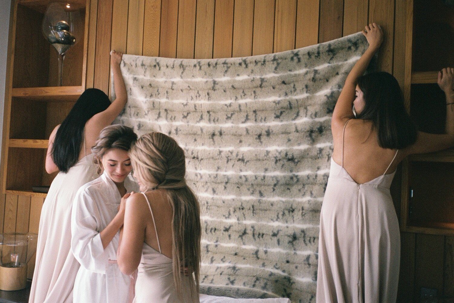 Wedding party members hang decorative fabric against wooden paneled wall.