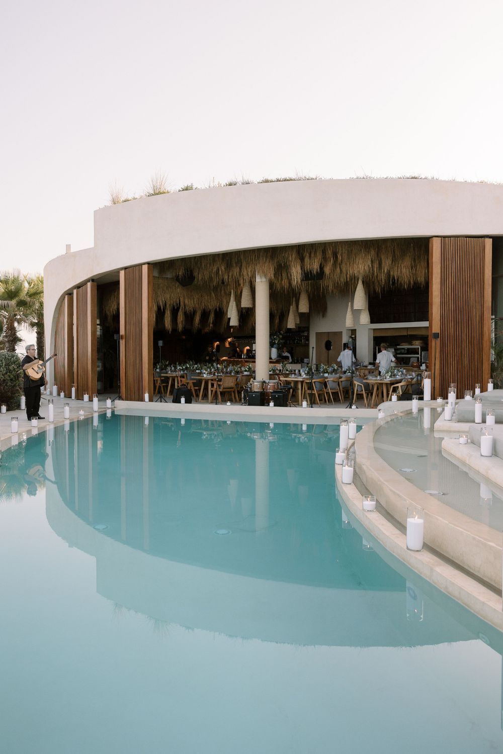 Modern curved swimming pool with thatched roof pavilion and lounging area at luxury resort.