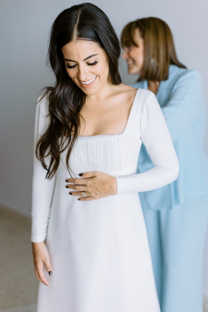 An elegant long-sleeved white dress being fitted in a bright minimal setting.