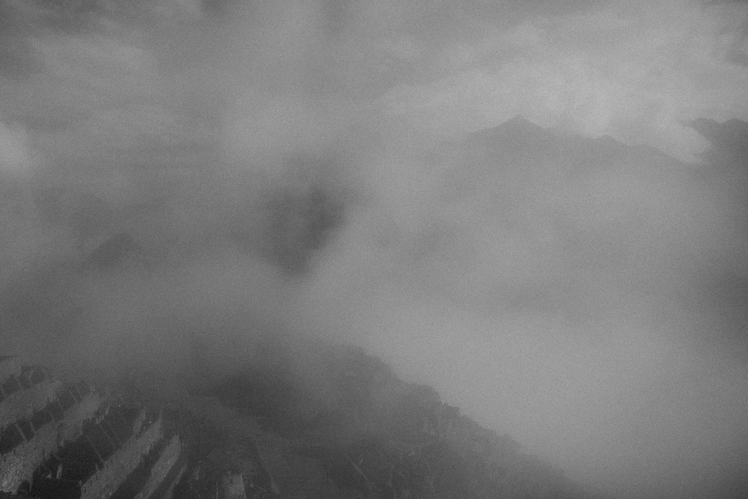 Misty mountain peak shrouded in atmospheric clouds and fog in dramatic black and white.