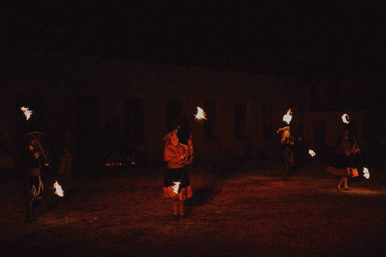 Fire performers create a dramatic nighttime display with flaming torches against a dark background.