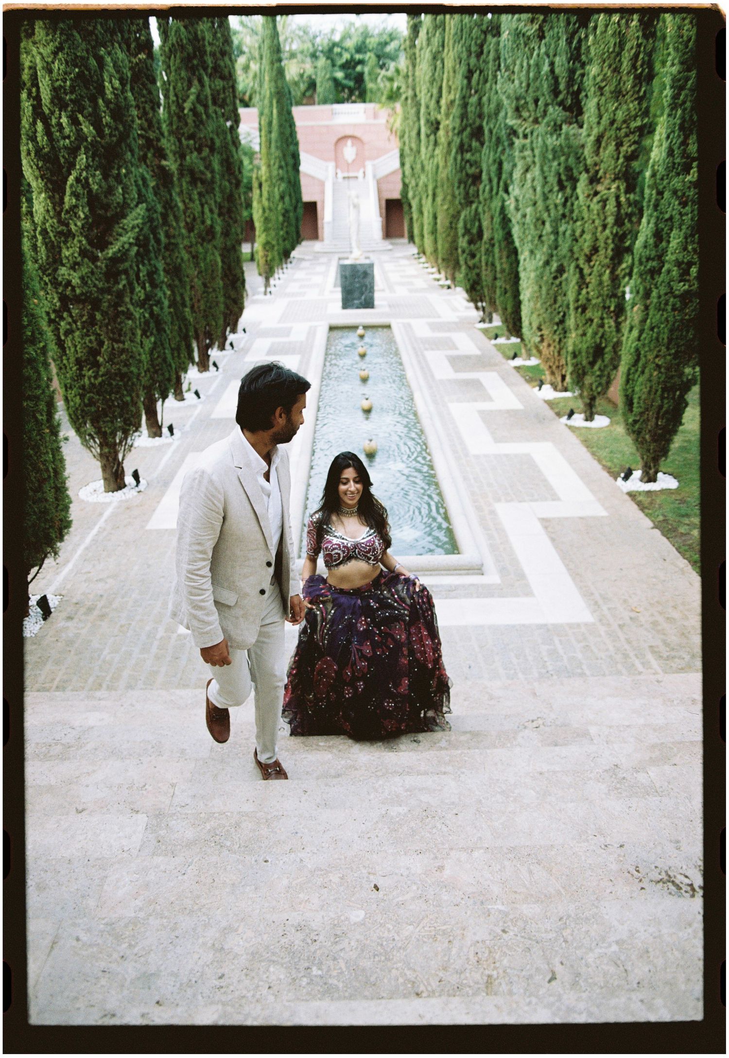 Elina and Jag climbing the garden staircase between tall cypress trees, photographed on film.