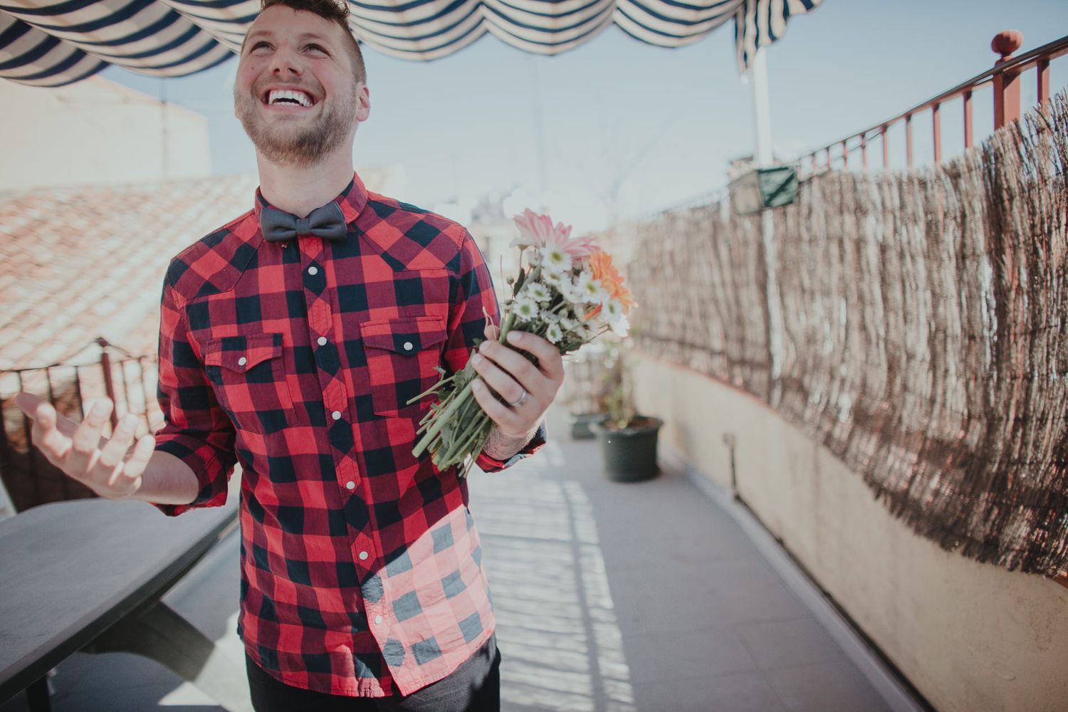 Person in red plaid shirt holding money on outdoor terrace with striped awning.