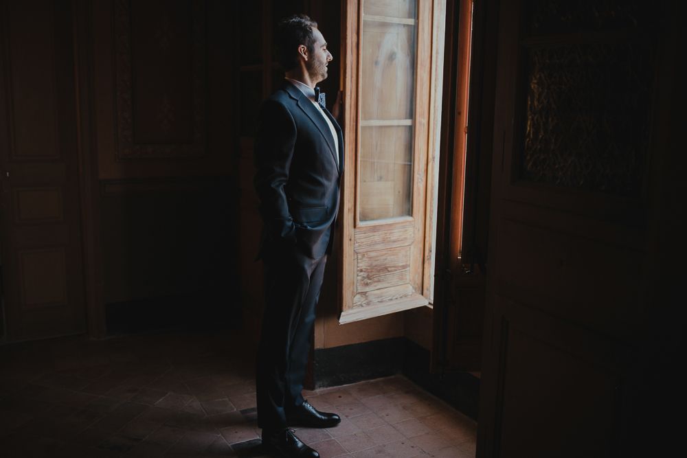 Elegant silhouette of a suited figure standing by a window in moody lighting.