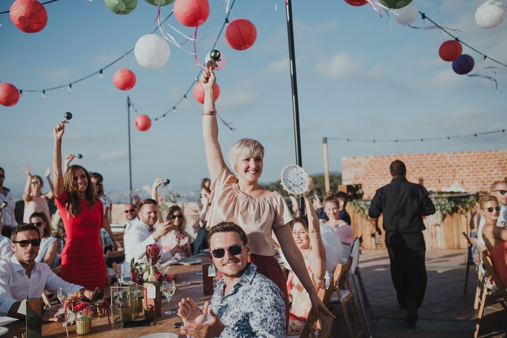 Festive outdoor party with red paper lanterns and people celebrating on a rooftop during daytime.