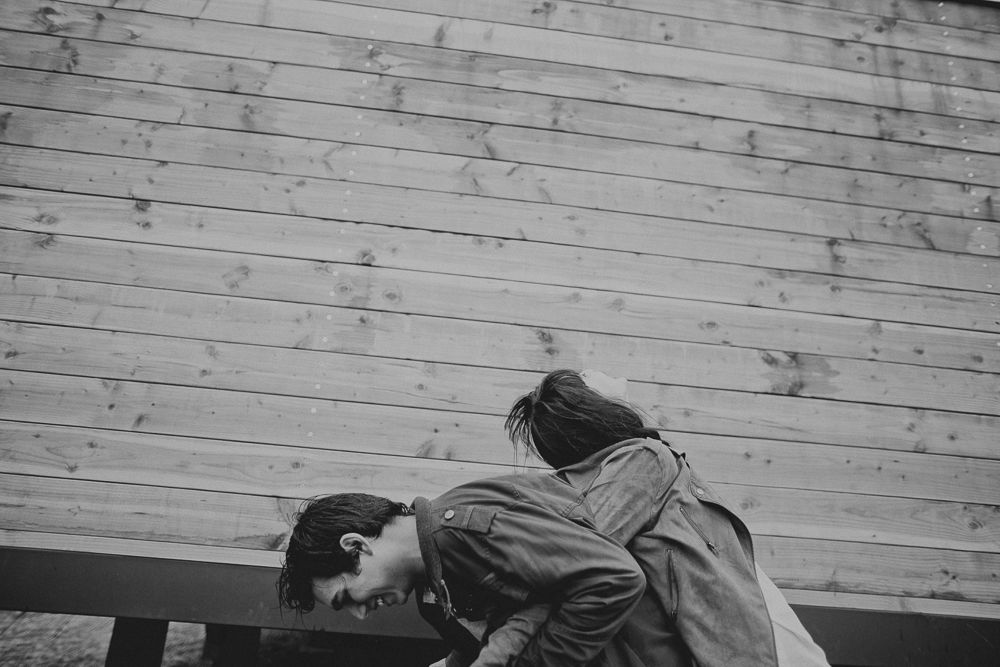 Two people share an intimate black and white moment on a bench against wooden planks.