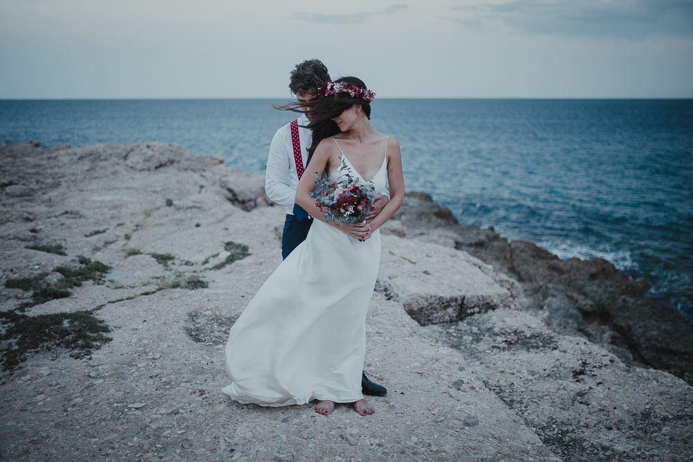 A romantic wedding portrait captures a couple on dramatic coastal rocks.