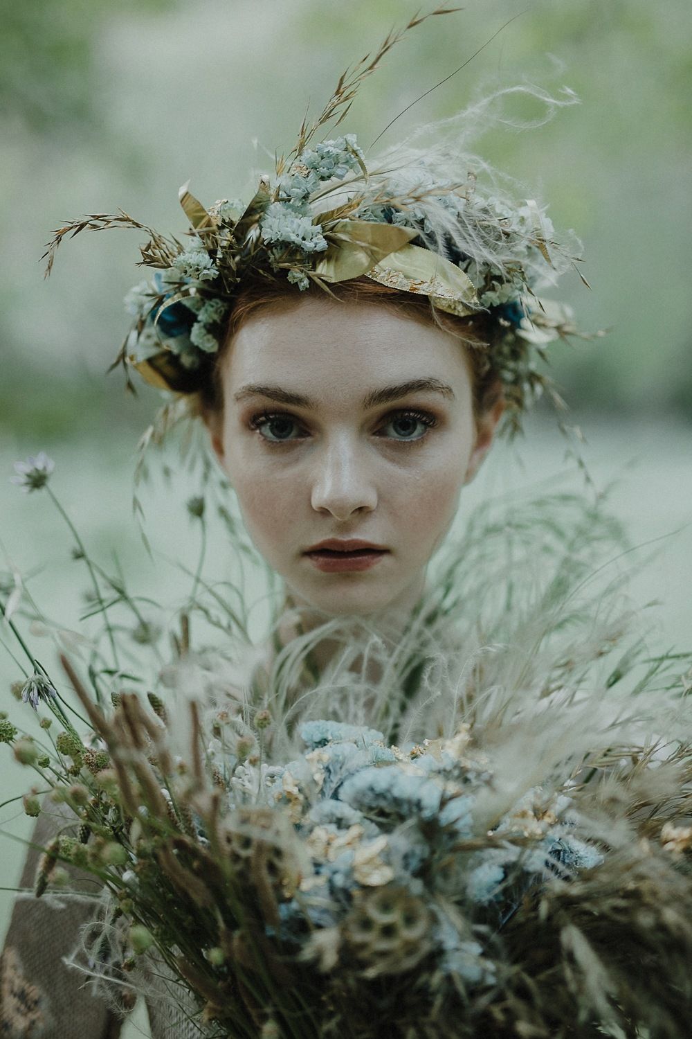 Close-up portrait featuring a nature-inspired crown with blue flowers and feathers.