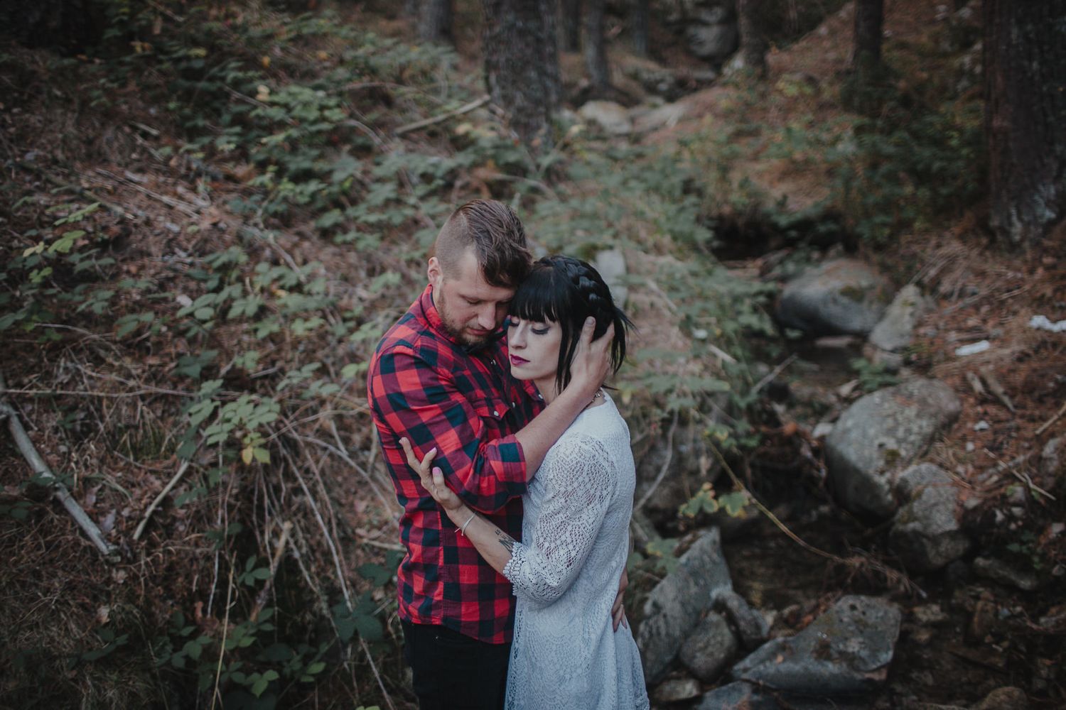 Couple sharing intimate moment among rocks and trees in forest setting.