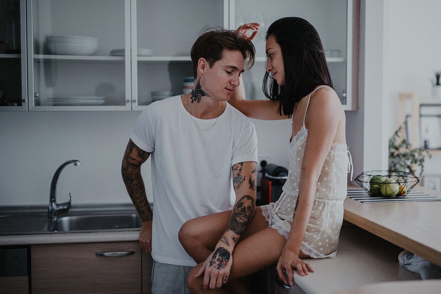 Couple sharing intimate moment in modern kitchen with white cabinets.