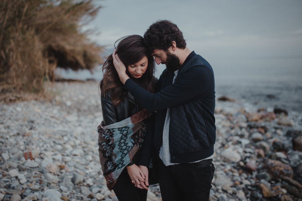 Intimate moment between a couple on a rocky beach during overcast weather.