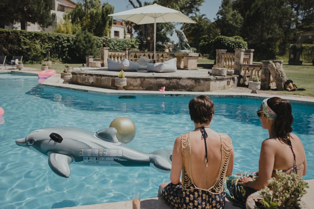 Pool scene with inflatable dolphin float and patio furniture beside clear blue water.