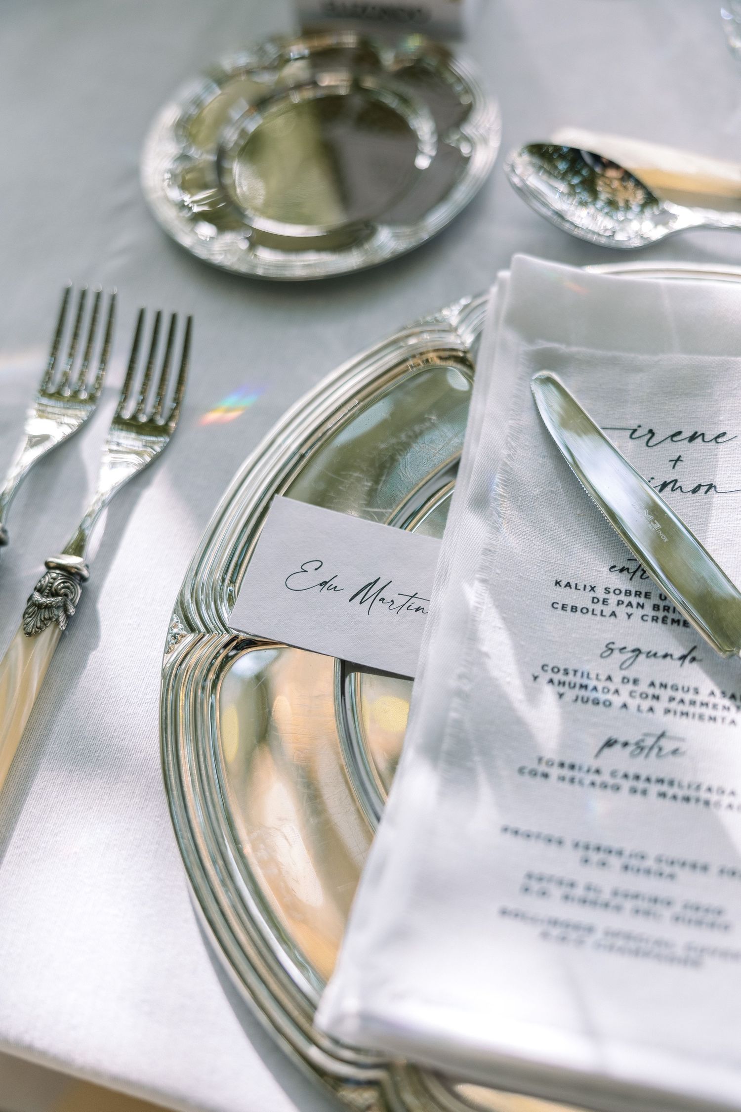 Close-up of refined wedding table setting with silver charger plates and calligraphy place cards.