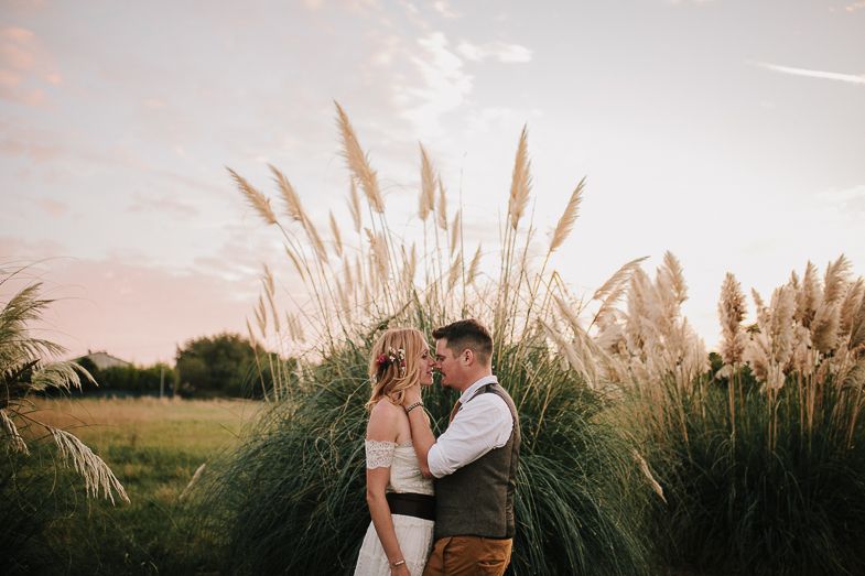 A couple stands together against beautiful pampas grass during sunset.