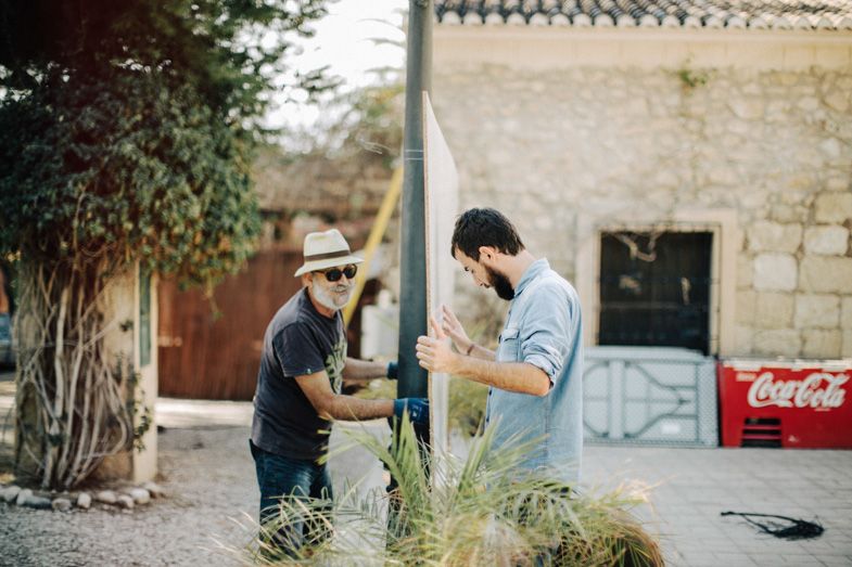 Two people working together on outdoor installation project near brick wall.