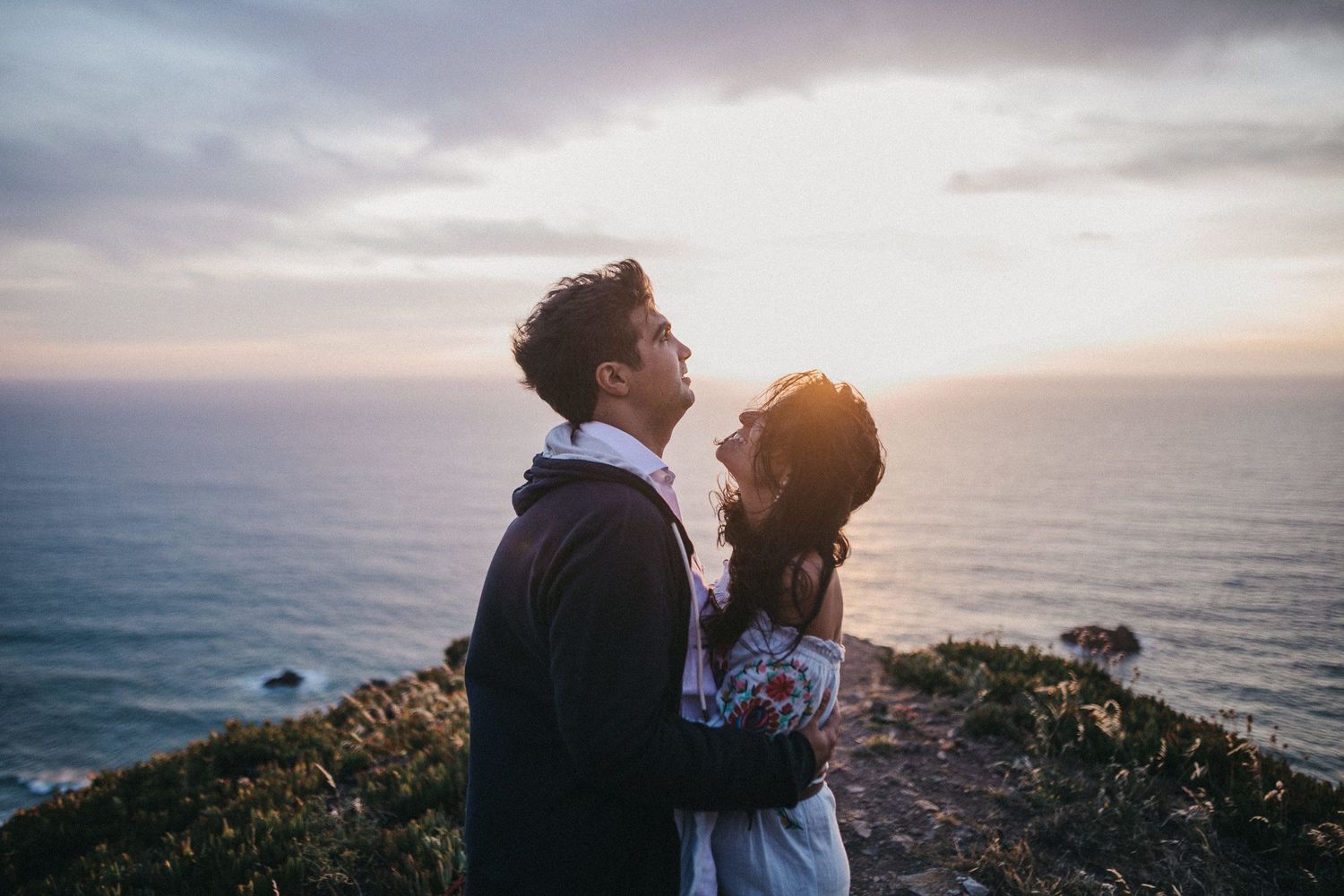 Couple admiring the ocean view together on a cliff during sunset.