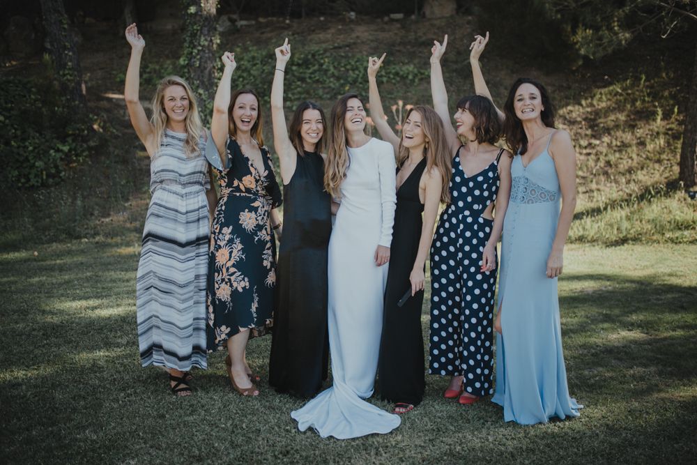 Group of women in formal dresses celebrating with raised arms outdoors.