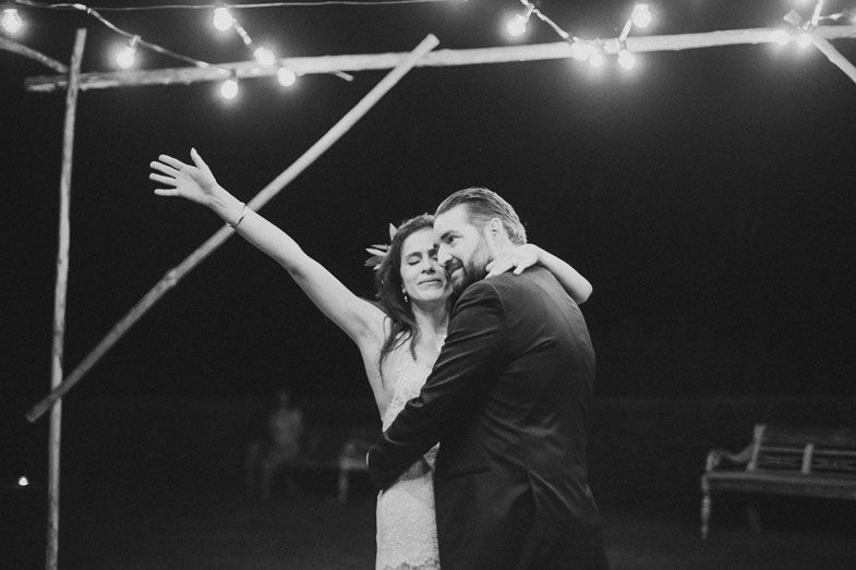 A couple dancing under string lights at their wedding reception in black and white.