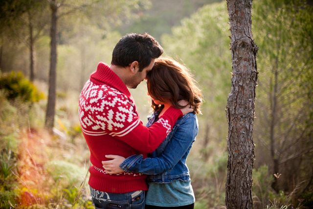 Romantic couple in matching red and denim outfits embracing near a tree in nature.