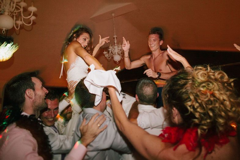 Partygoers lift a bride in white dress during an energetic wedding reception celebration.