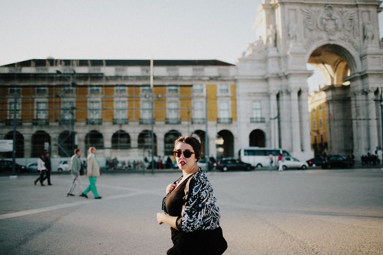A visitor poses in front of an elegant archway and yellow colonial architecture in a European plaza.
