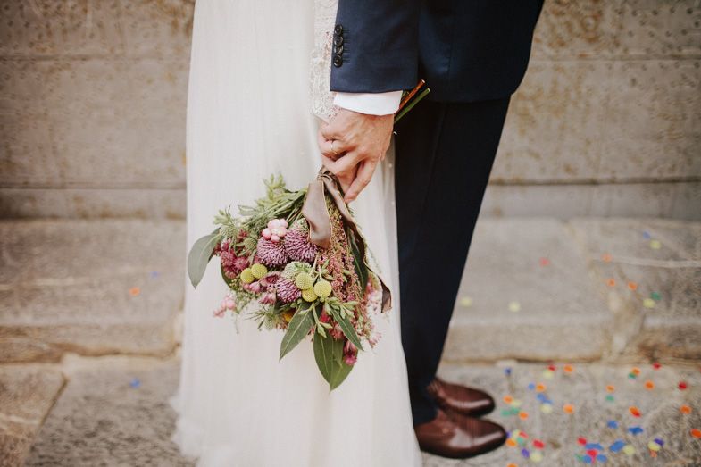 Close-up of couple holding a rustic wedding bouquet with stone wall background.