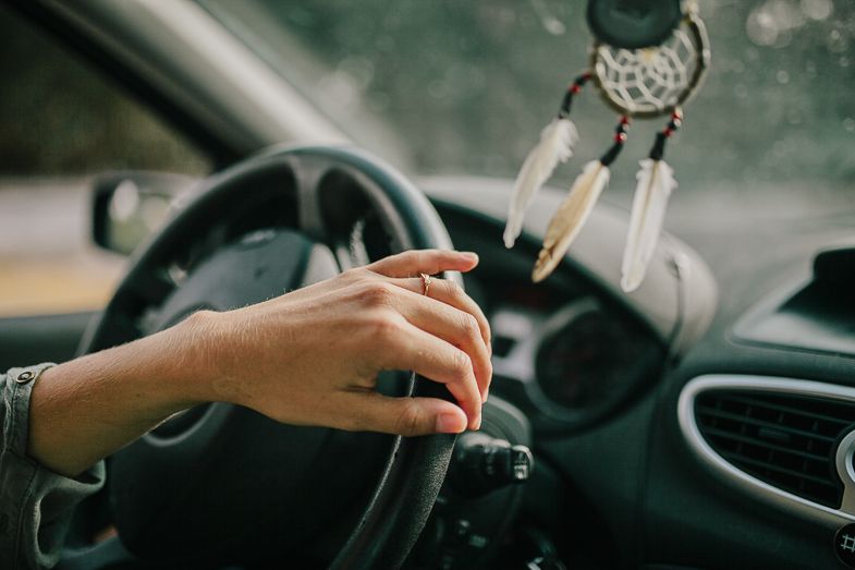Hand gripping a steering wheel inside a car with keys hanging from the ignition.