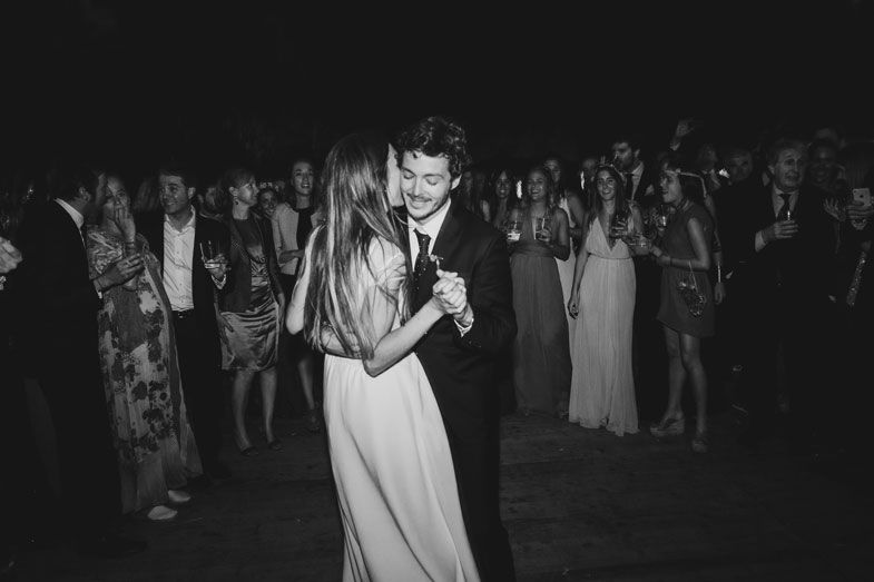 A couple shares their first dance at a nighttime wedding reception surrounded by guests.