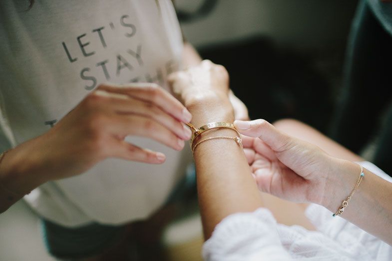 Close-up of hands putting on a delicate bracelet with text reading 'Let's Stay'.