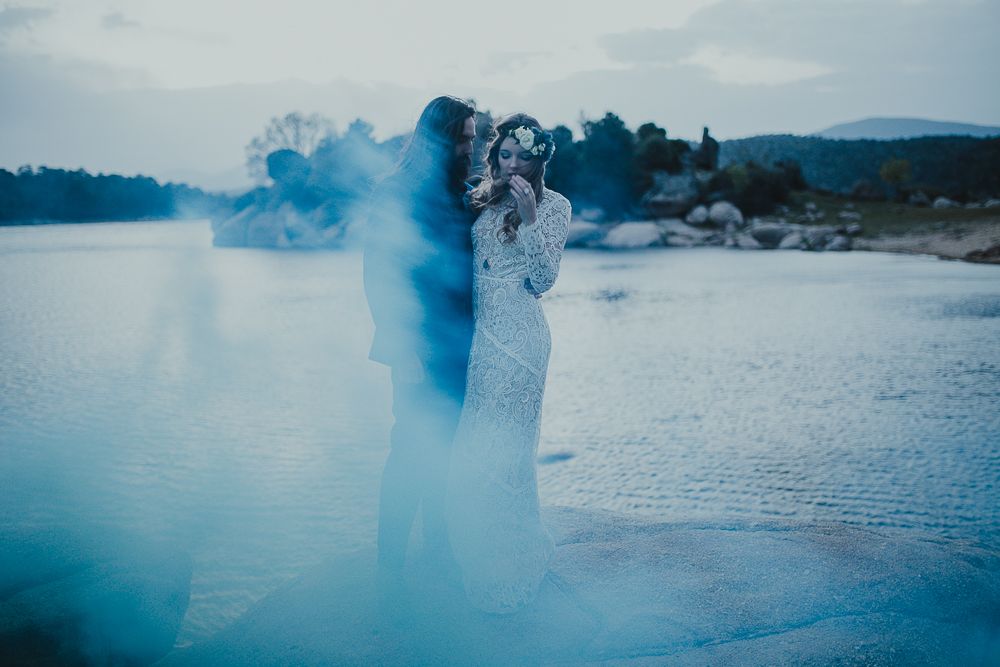 Dreamy wedding photoshoot with blue smoke effects near a tranquil lake.