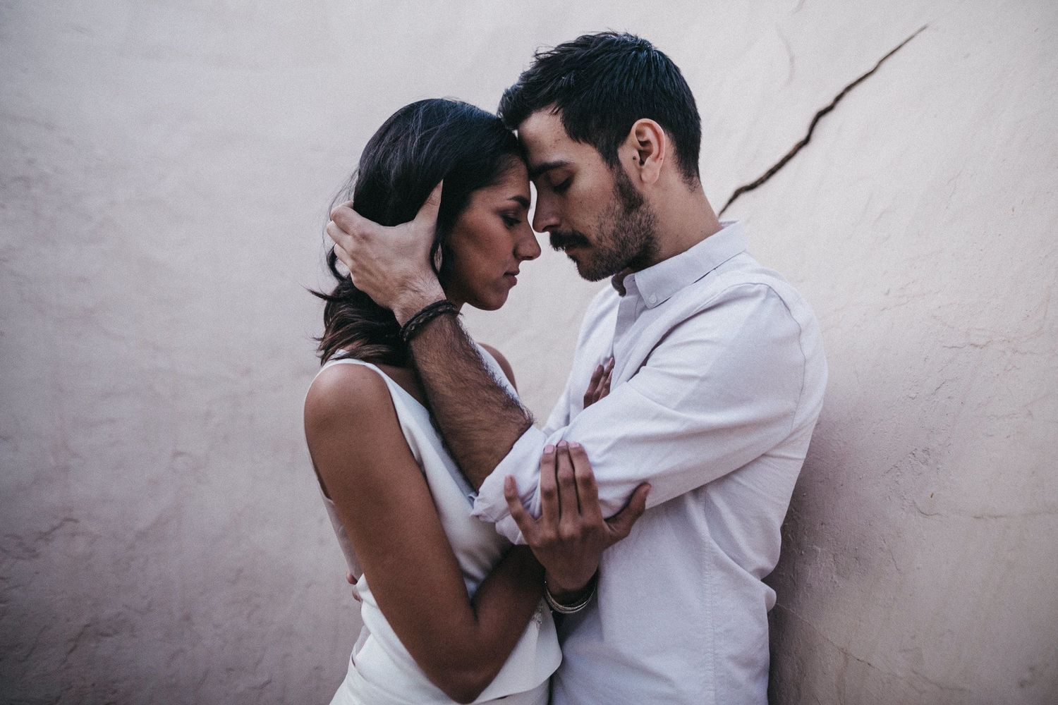 Tender moment captured between a couple in white attire against a light background.