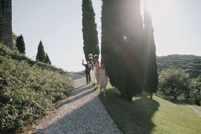Newlyweds walking down cypress-lined path in Italian countryside.